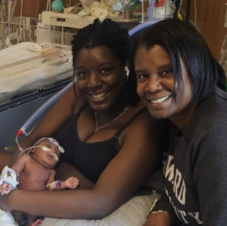 Mom and grandma smiling together holding tiny baby Renee in the PCICU